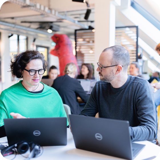 two colleagues working sitting laptops talking square 