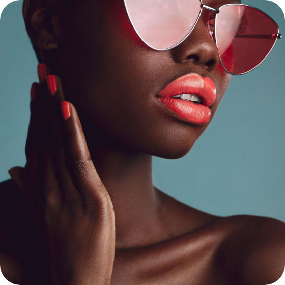 Schwarzes Modell, das eine Sonnenbrille mit leuchtend orangefarbenem Lippenstift und Nägeln modelliert