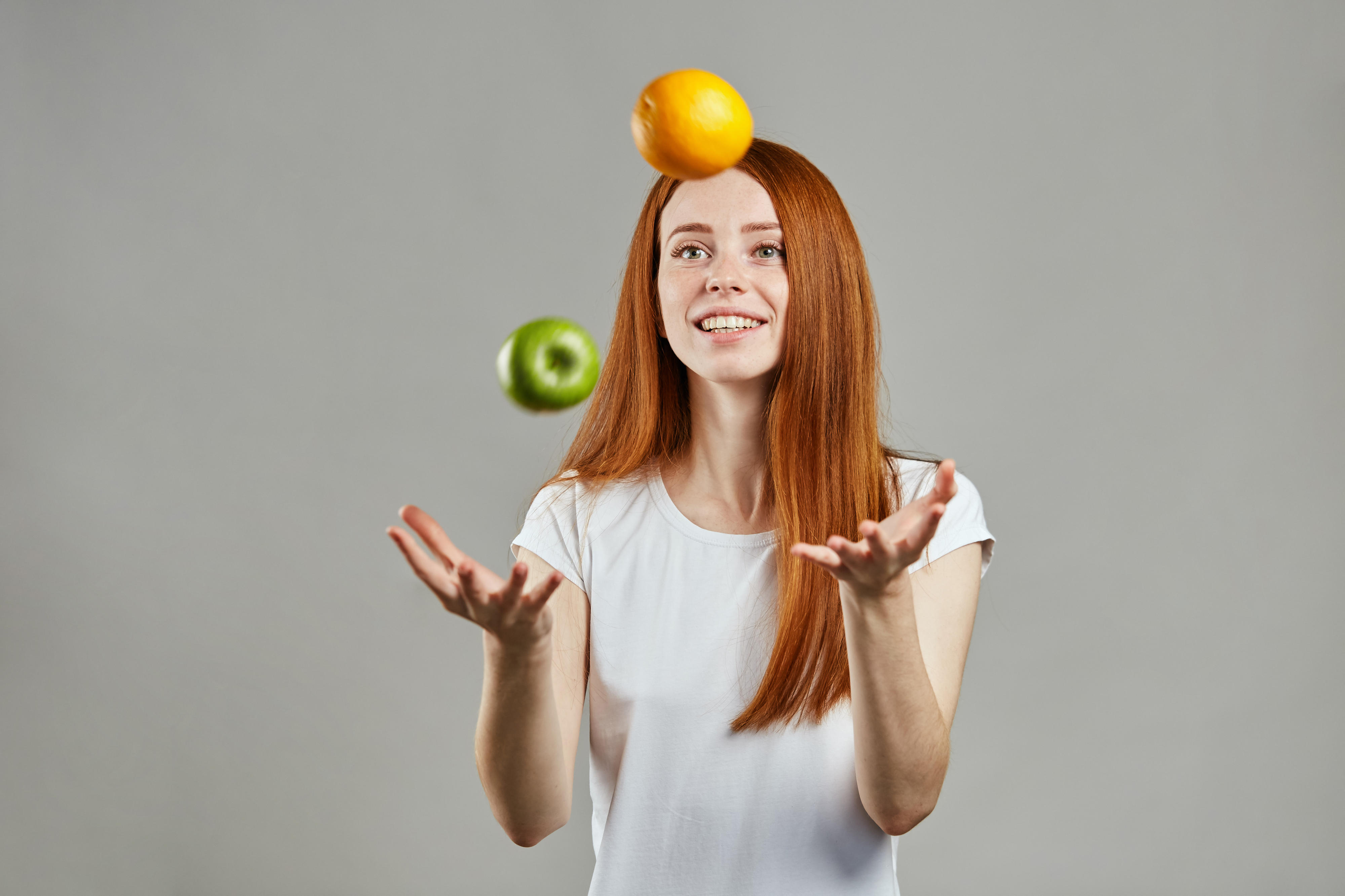 Young woman juggling with apple and orange
